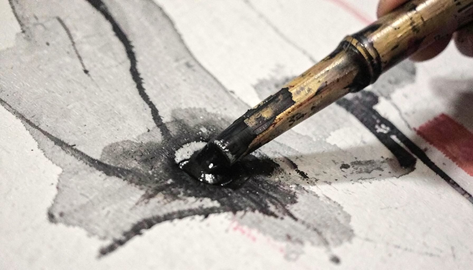 Close-up of a bamboo hand-poke tool pressing ink into skin, muted charcoal tones with subtle warm highlights on the tool tip.